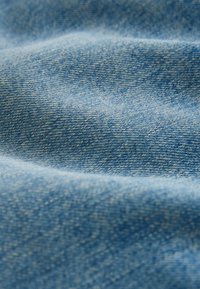 Primer plano de tela de mezclilla azul texturizada con patrón de tejido visible y pliegues suaves que crean sombras tenues.