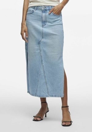 Hellblauer Denim-Midirock mit diagonaler Naht vorne, Seitenschlitz, getragen mit schwarzen Knöchelriemen-Pumps und einem teilweise sichtbaren weißen Oberteil.