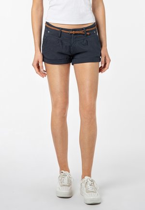Marineblaue Baumwollshorts mit vorderen Falten, geflochtenem, braunen Gürtel und zwei Taschen. Kurze Länge und umgeschlagener Saum. Weiße Sneakers getragen.