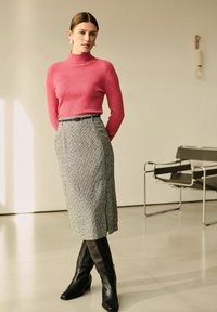 Ribbet rosa turtleneck, grå mønstret blyantskirt med sideslids og sorte knæhøje hæle støvler, der skaber en tætsiddende silhuet.