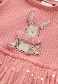 Tissu côtelé rose avec un lapin brodé portant un col en tulle rose, au-dessus d'une jupe froncée avec des pois dorés.
