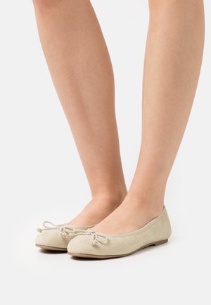 Ballerines en suède beige avec un bout rond et un nœud décoratif en cordon torsadé à l'avant. Semelle plate et design minimaliste.