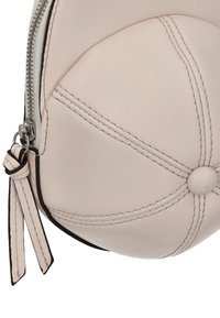 Kerek krémszínű bőrtáska látható varrással és középen díszítő gombbal. Ezüst cipzárral és levehető pánttal rendelkezik.