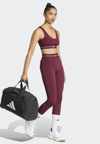 Top deportivo y leggings burdeos con detalles del logo de Adidas en blanco; bolsa de deporte negra con un gran logo blanco; calcetines blancos; zapatillas deportivas.