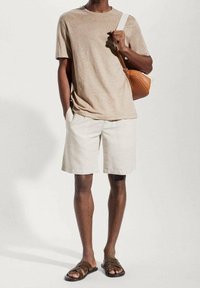 T-shirt beige à manches courtes, short crème, sandales slides marron. Porte un sac bandoulière couleur tan. Coupe simple et décontractée, tissu léger, sans motifs.