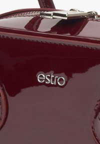 Bordeaux patenten leren handtas met een gladde textuur, voorzien van een zilveren "estro" logo en minimalistische designelementen.