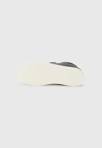 Svart sneakers med teksturert design, med hvit gummisåle. Sålen er mønstrete for grep, og fremhever holdbarhet og trekkraft.