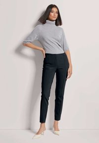 Grijs coltrui met korte mouwen, gecombineerd met zwarte slim-fit broek met zijnaad. Het model draagt witte hakken.