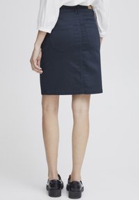 J�ūras spēku zila džinsa svārku ar taisnu griezumu, divām aizmugurējām kabatām un vidējas augstuma vidukli. Tam ir tīras šuves un maiga tekstūra.