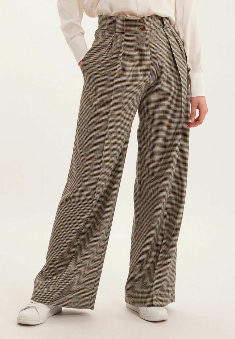 Pantalons larges à carreaux dans des tons marron et beige, dotés d'une taille haute, de plis et de deux boutons, associés à des baskets blanches.
