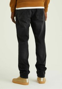 Svarta denimjeans med rak passform, två bakfickor och uppvikta nederkanter. Kombinerade med ljusbruna sneakers.