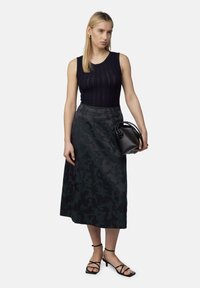 Schwarzes geripptes Tanktop, langer Rock mit dunklem Muster und schwarze Riemchen-Heels. Accessoire: kleine schwarze Handtasche mit runden Griffen.