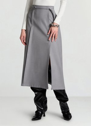 Jupe midi grise avec un détail ceinture, ornée de plis et d'une fente latérale. Associée à des cuissardes noires brillantes. Texture de tissu lisse et formel.