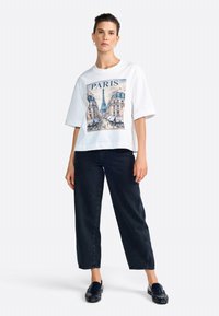 T-shirt en coton blanc avec un graphique coloré de Paris, coupe décontractée et manches larges. Associé à un pantalon en denim foncé et des mocassins noirs.
