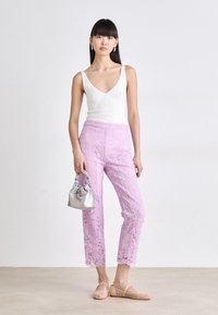 Roze kanten broek met golvende zoom, gecombineerd met een witte geribbelde tanktop en beige mesh instappers. Een zilveren geplooide handtas maakt de look compleet.