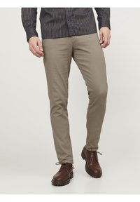 Pantalon beige coupe slim, confectionné dans un tissu lisse. Associé à des bottes à lacets marron, avec un bout arrondi et une semelle texturée.