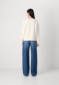 Cremefarvet oversized sweatshirt med lange ærmer, parret med højtaljede, brede blå jeans. Glat tekstur, minimalistisk design og afslappet pasform.
