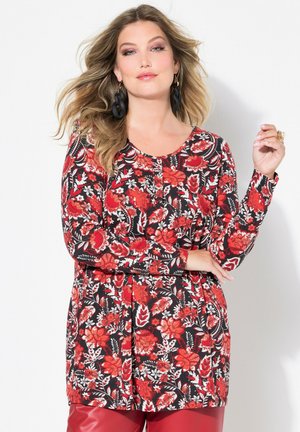 Haut à manches longues fleuri en noir, avec des motifs rouges et blancs, col rond et tissu doux. Associé à un pantalon rouge brillant.