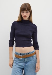 Marineblauer Rippen-Strickpullover mit Rollkragen und dreiviertellangen Ärmeln, kombiniert mit hoch taillierten hellblauen Jeans und einem braunen Gürtel.