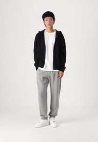 Sudadera negra con cremallera, camiseta blanca, pantalones de chándal grises y zapatillas blancas. Ropa informal con tejidos de mezcla de algodón y acentos de ribete en el dobladillo.