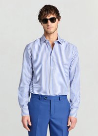 Gestreiftes blau-weißes Hemd mit langen Ärmeln und Button-Down-Kragen, kombiniert mit einer blauen Hose. Sonnenbrille sorgt für einen Kontrast.