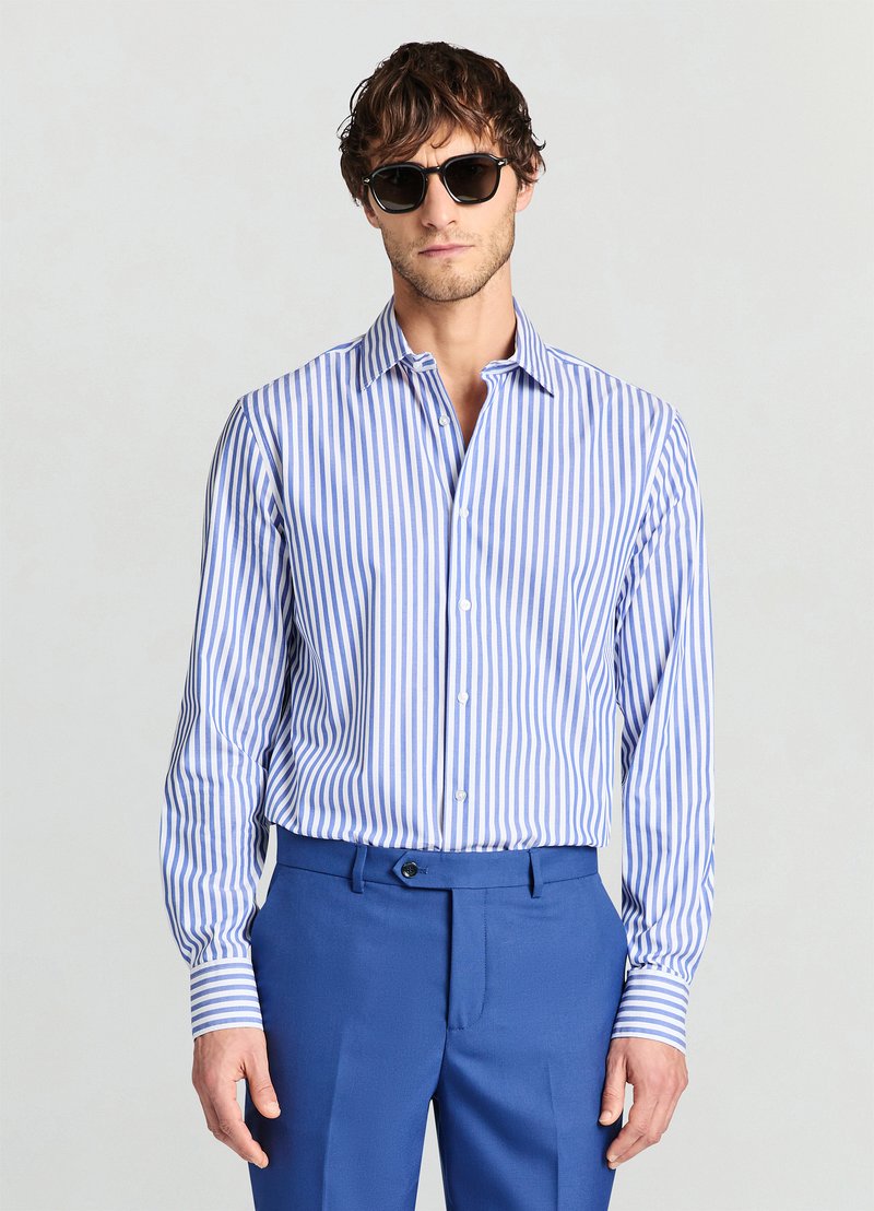 Gestreiftes blau-weißes Hemd mit langen Ärmeln und Button-Down-Kragen, kombiniert mit einer blauen Hose. Sonnenbrille sorgt für einen Kontrast.