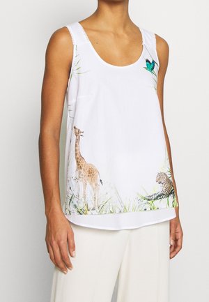 Femme portant un haut blanc sans manches avec des illustrations d’une girafe, d’un léopard, de feuillage vert et d’un oiseau bleu sur le devant.