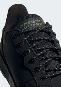 Sneaker nera da atletica con tomaia testurizzata, presenta dettagli in rete, occhielli esagonali e lacci intrecciati. Branding verde sulla linguetta.