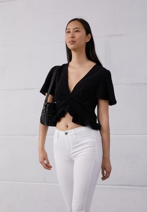 Top preto de manga curta e cropped com decote em V profundo e bainha com babado, combinado com jeans skinny brancos e uma mala preta texturizada.