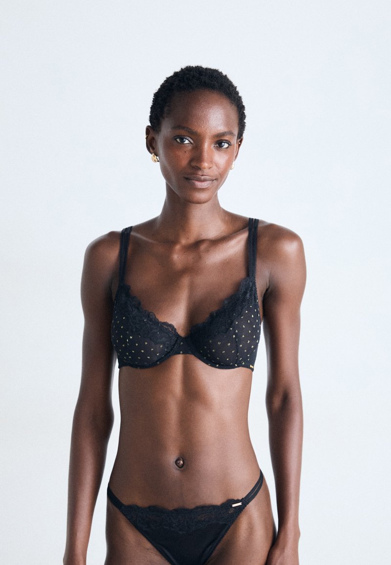 Ensemble de lingerie en dentelle noire comprenant un soutien-gorge à pois dorés et un bas de bikini assorti, mettant en valeur des finitions en dentelle détaillées et des fines bretelles.