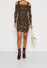 Černé květinové bodycon šaty s dlouhými rukávy, výstřihem odhalenými rameny a řasenými detaily. Doplněné o bordó kotníkové boty a béžovou kabelku.