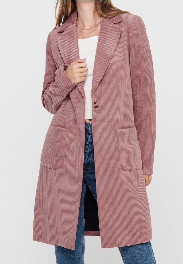 Pink corduroy long blazer with notch lapels, two front pockets, and a single button closure, worn over a white top and blue jeans.