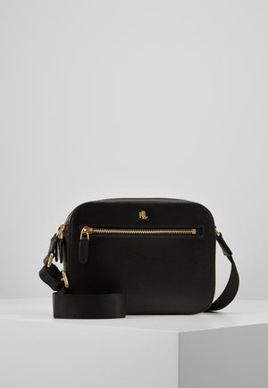 Borsa a tracolla rettangolare nera con cerniera e logo dorati, superficie testurizzata e tracolla regolabile appoggiata su un piedistallo bianco.