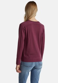 Bordó svetr vyrobený z měkké pleteniny, s kulatým výstřihem, dlouhými rukávy a ribbovaným lemem. Spárován se světle modrými džíny.