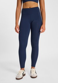 Leggings blu navy a vita alta realizzati in tessuto elasticizzato, caratterizzati da una texture liscia e un design alla caviglia, abbinati a sneakers chiare.