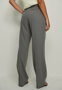 Lettihousut vaaleanharmaasta kankaasta, joissa on sileä pinta, korkea vyötärö ja takataskut, yhdistettynä mustiin sandaaleihin.