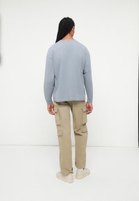 Šviesiai mėlyna ilgarankovė marškinėliai, laisvas pjūvis, derinami su smėlio spalvos kroso kelnėmis, turinčiomis kelis kišenes, užsidėti su šviesiomis bateliais.