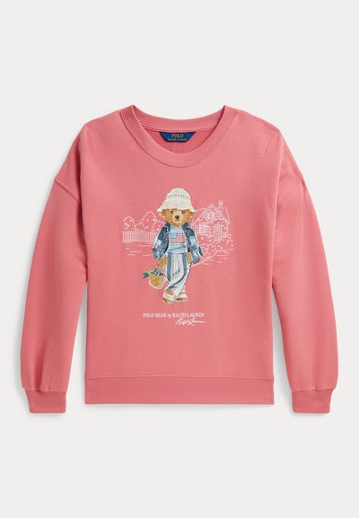 Ροζ φούτερ με μια αρκούδα που φοράει καπέλο, τζιν μπουφάν, ριγέ παντελόνι, κρατώντας ένα καλάθι, με σκίτσα σπιτιού και κήπου στο φόντο.