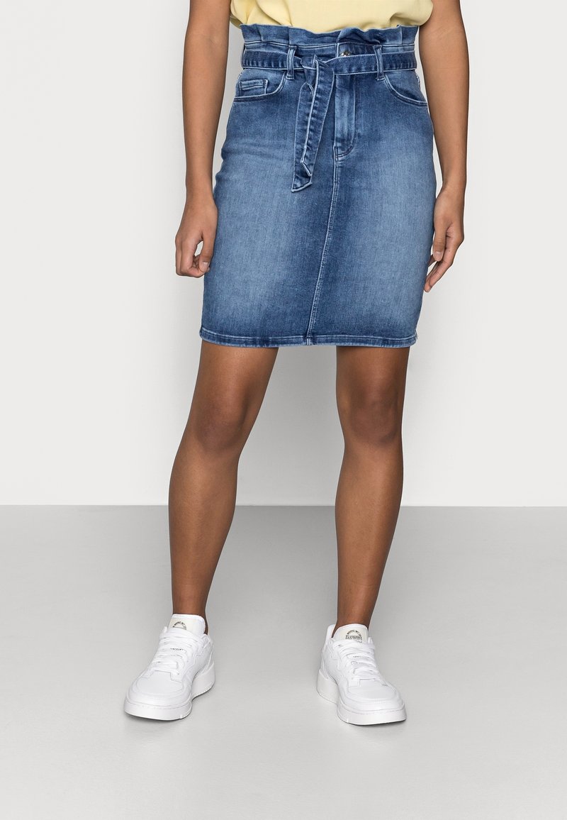 Denimkjol med hög midja och bälte, blåtvätt, två framfickor, rak skärning och fåll ovanför knäna, matchad med vita sneakers.