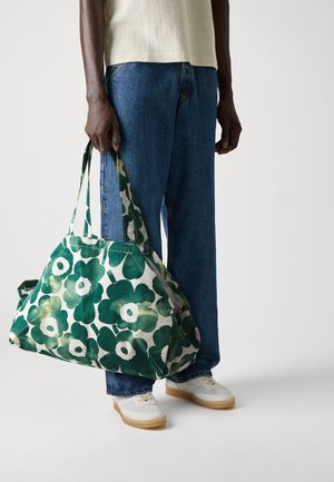 Green floral pattern bag made of cotton fabric, featuring two sturdy handles and a spacious design, shown in the hands of a person.