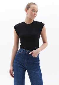 Top senza maniche a righe nere abbinato a jeans in denim blu a vita alta. Il top presenta un colletto rotondo e una silhouette aderente.