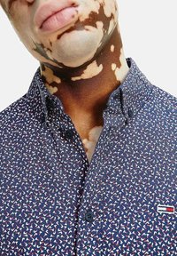 Camicia blu navy con bottoni caratterizzata da un tessuto testurizzato con un piccolo motivo astratto ripetuto in bianco e rosso; include un logo sul petto.