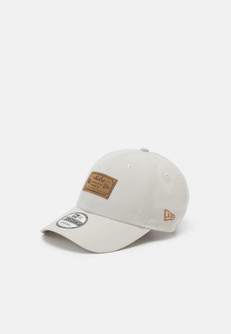 Light gray cap with a brown leather patch on the front, featuring stitched details and a curved brim. Small logo on the side.