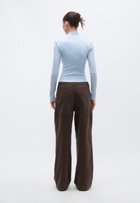 Ανοιχτό μπλε μακρυμάνικη μπλούζα και καφέ παντελόνι με φαρδιά μπατζάκια, με πίσω τσέπες και λείο υλικό, εμφανίζεται από πίσω.