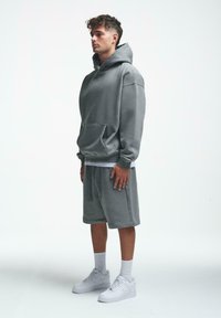 Grå oversized hettegenser med kengurulomme, kombinert med matchende shorts. Brukt med hvite joggesko og ankelhøye sokker. Jevn tekstur.