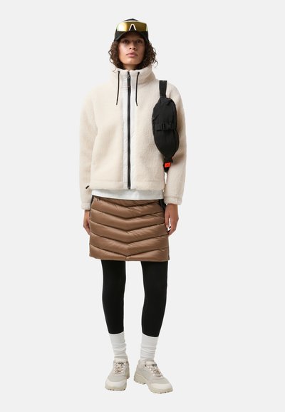 Fleecejakke i creme, luftig brun nederdel med fiskebensmønster, sort skuldertaske, leggings, hvide sokker og lyse sneakers.