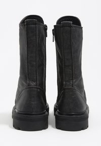 Para czarnych skórzanych kozaków do połowy łydki z bocznymi suwakami i masywnymi gumowymi podeszwami, widziane od tyłu na białym tle.