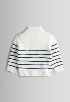 Balts adīts džemperis ar tumši ziliem horizontāliem svītrām, augstu apkakli un ribojumu piedurknēm un apakšmalai. Raksturo mīksta faktūra un ikdienišķs dizains.