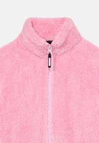 Rožinis fliso švarkas su aukštu apykakle, visiškai užtraukiama priekyje ir tekstūruotu paviršiumi. Pasižymi minkštu, puriu audiniu ir juodu užtrauktuko traukimo žiedu.