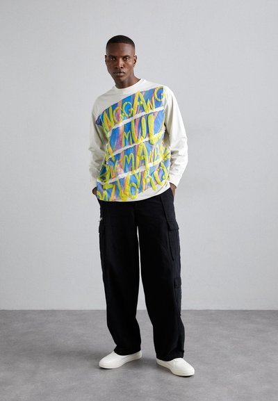 Tricou alb cu mâneci lungi, având un text grafic multicolor pe partea din față. Combinat cu o pereche de pantaloni largi negri de tip cargo și adidași albi.